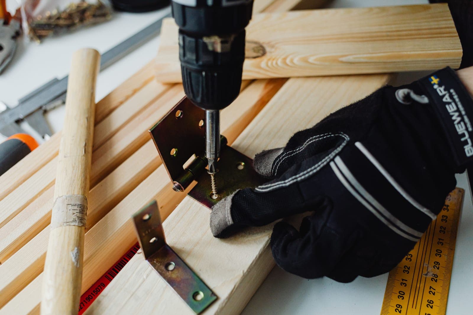 Power drill, metal bracket and work gloves laid out on lumber
