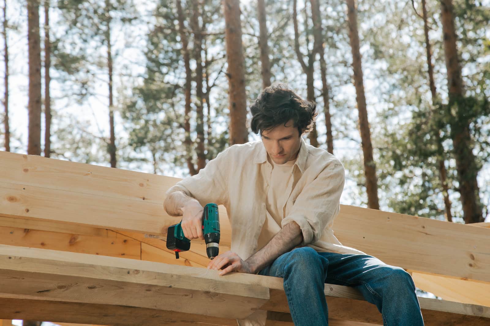 Carpenter driving screws into wooden beams outdoors with a power drill