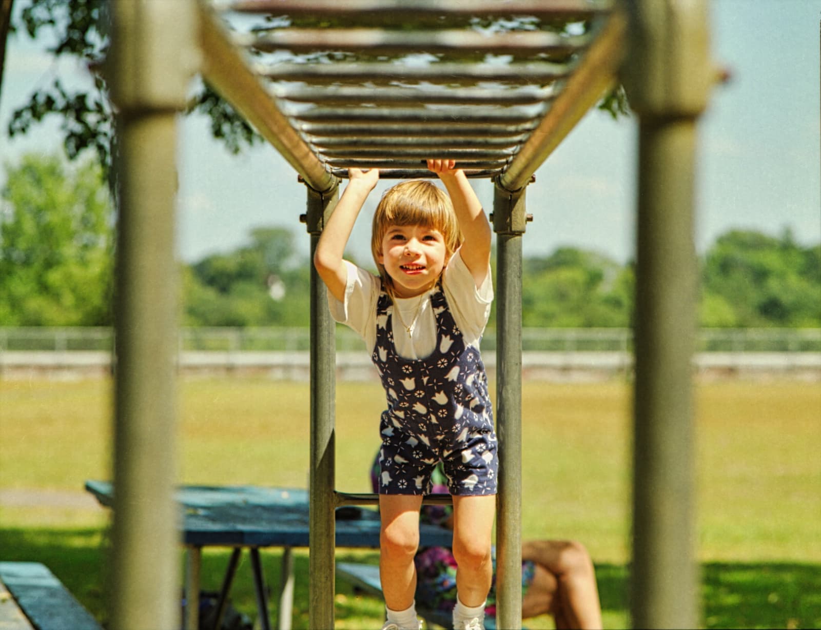 Young girl hanging from monkey bars at a sunny park