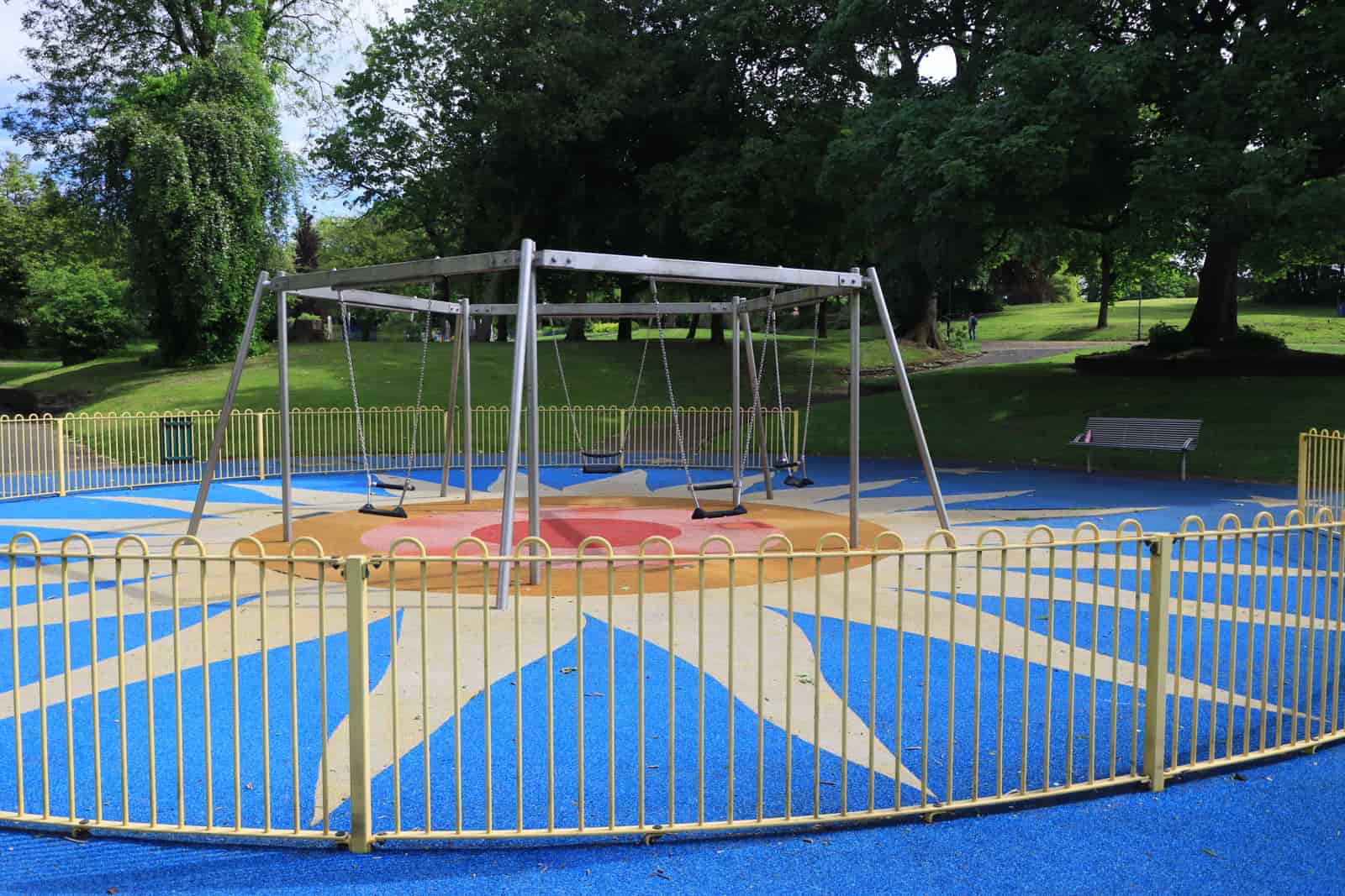 Empty metal-frame swings inside a fenced green park