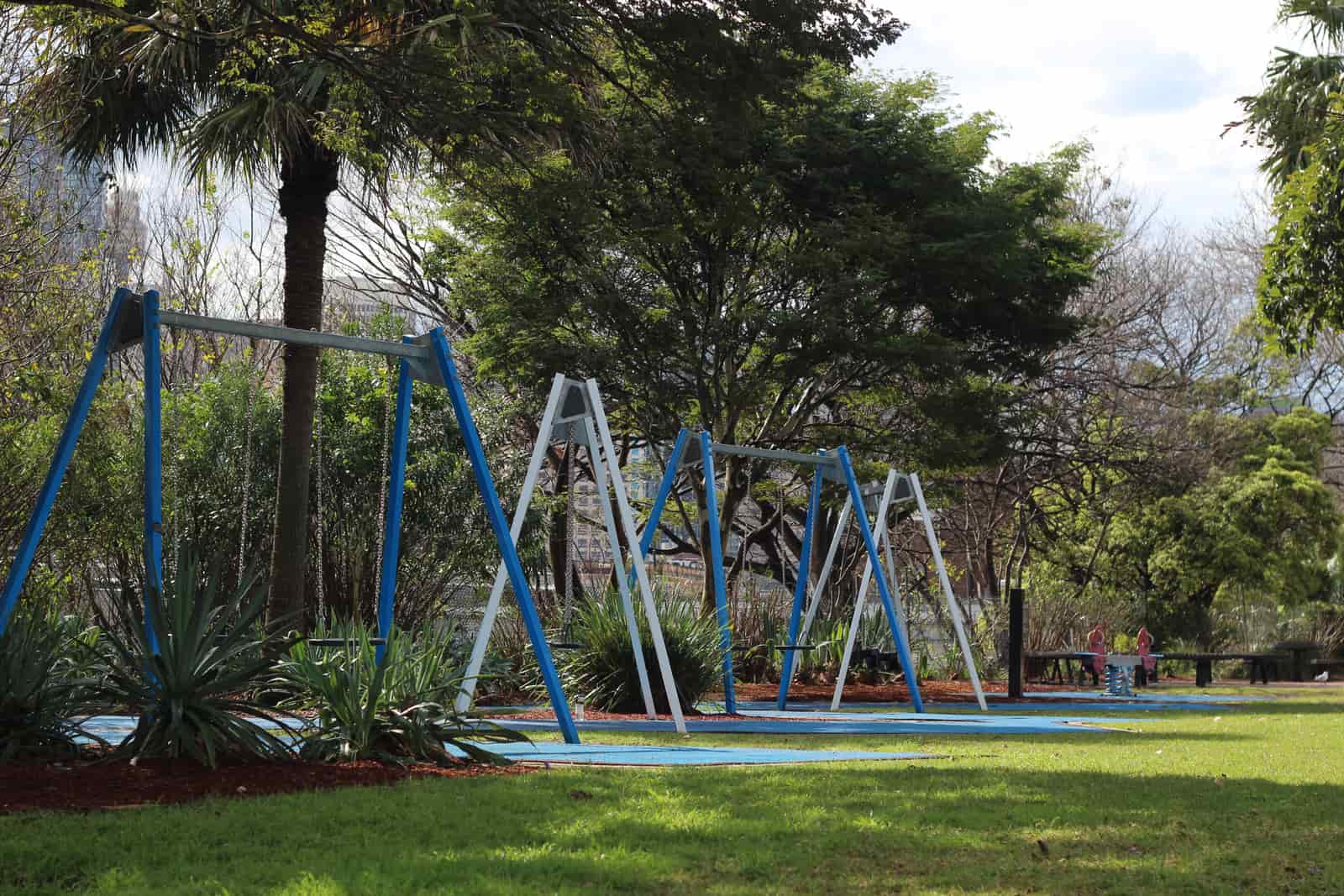 Swings in a sunny park playground surrounded by trees