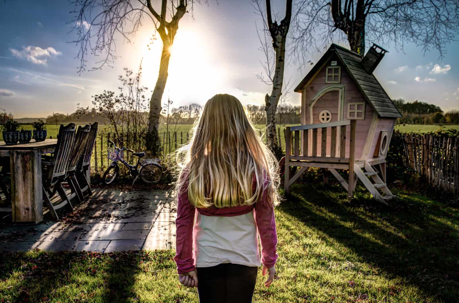 Child in a backyard beside a wooden playhouse under trees