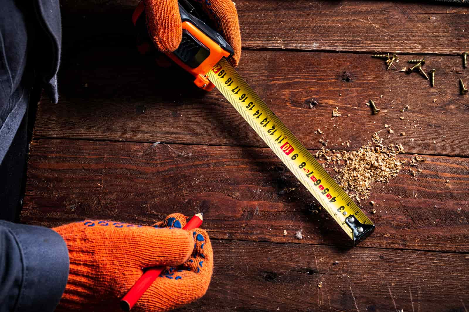 Gloved hands holding a tape measure against a wooden board