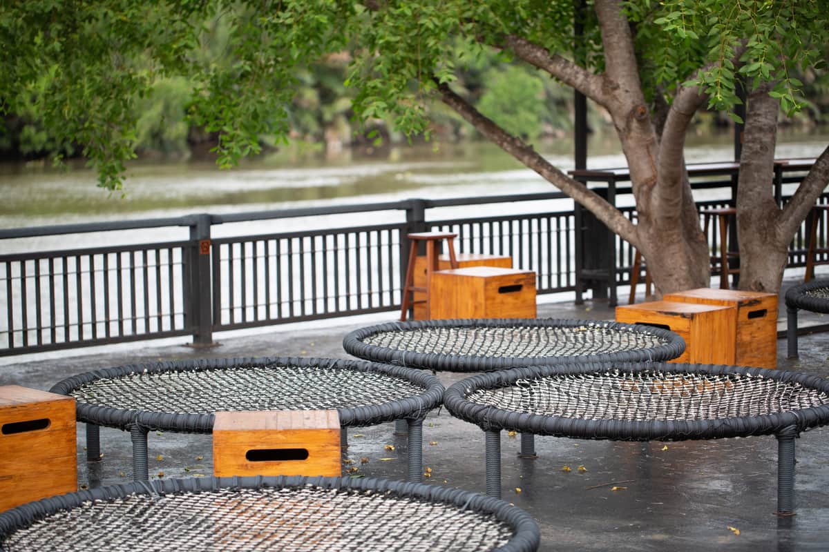 Round trampolines set flush into the ground beside wooden seats under trees