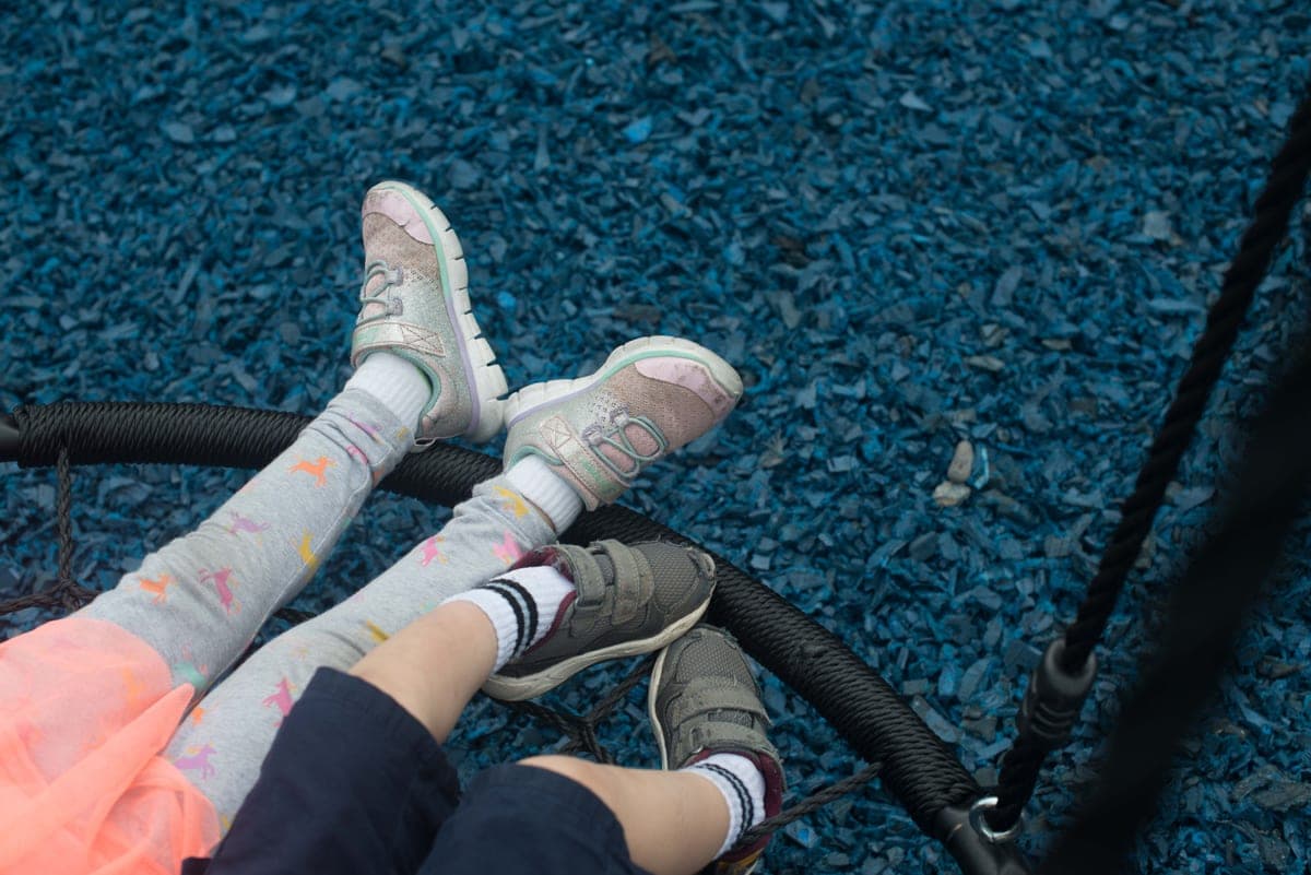 Two children on a swing over blue rubber mulch