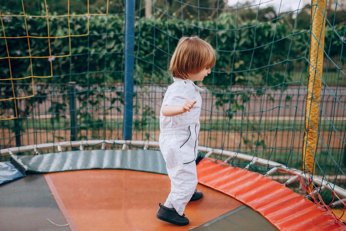 Young child in overalls standing on a round backyard trampoline