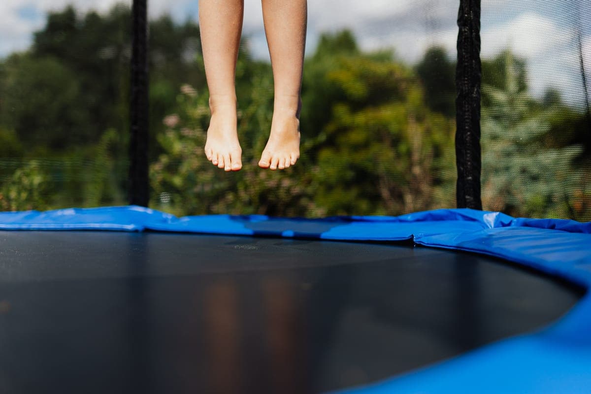 Child's bare feet mid-jump on a trampoline mat in summer light
