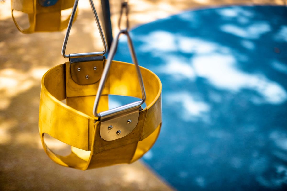 Close-up of a yellow swing seat and its chains in a sunlit park