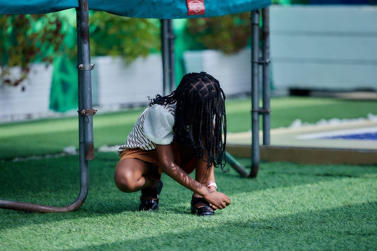 Girl crouching on artificial turf beside play equipment in summer