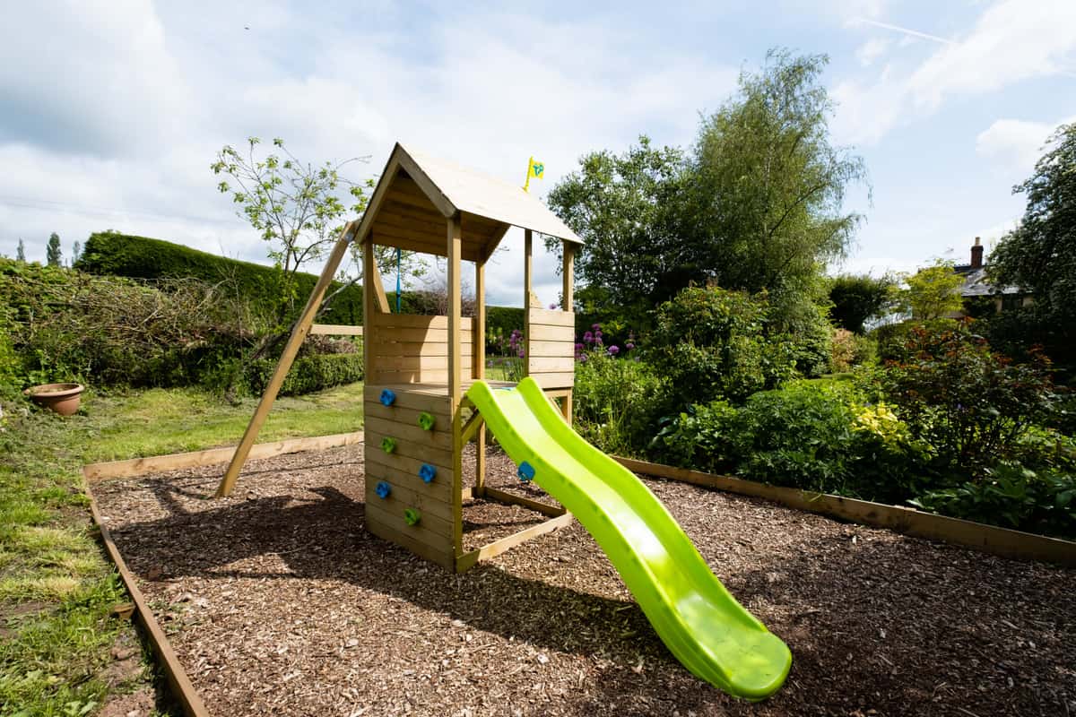 Wooden play structure with a slide in a leafy garden