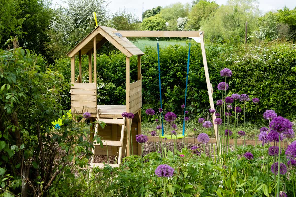 Wooden swing set in a garden surrounded by blooming alliums
